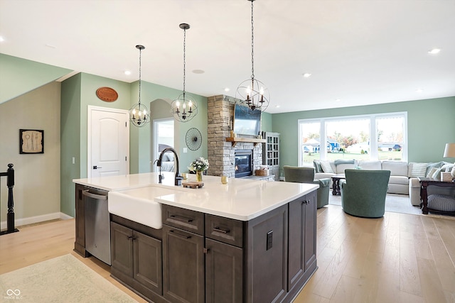 kitchen featuring a stone fireplace, light wood-type flooring, sink, dishwasher, and a kitchen island with sink