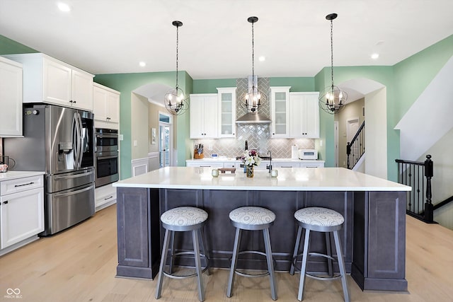 kitchen featuring stainless steel appliances, white cabinetry, light wood-type flooring, pendant lighting, and an island with sink