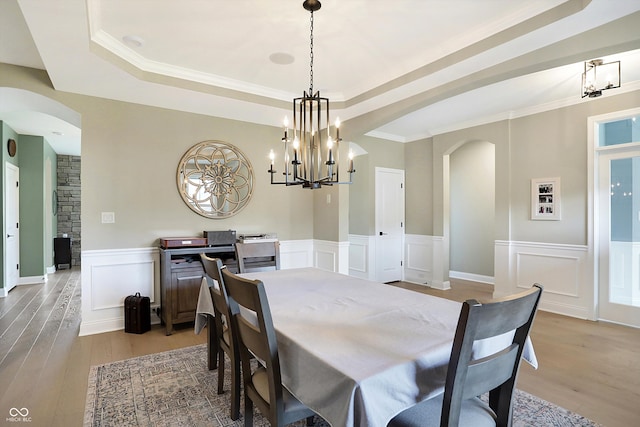 dining space featuring an inviting chandelier, a raised ceiling, light wood-type flooring, and ornamental molding