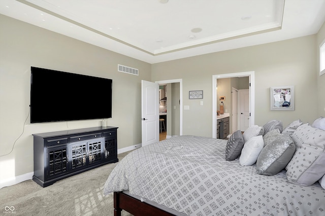 carpeted bedroom featuring ensuite bathroom and a raised ceiling