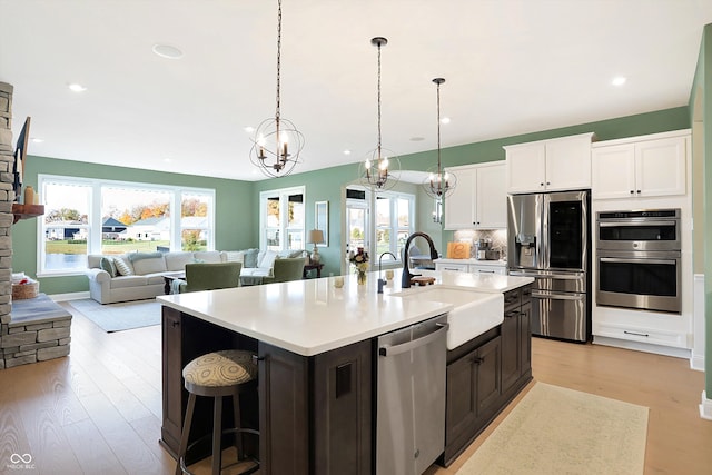 kitchen with light hardwood / wood-style floors, hanging light fixtures, sink, a kitchen island with sink, and appliances with stainless steel finishes