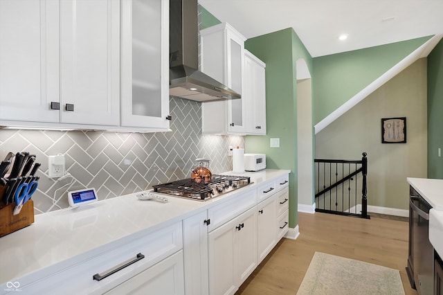 kitchen featuring light hardwood / wood-style floors, backsplash, stainless steel gas stovetop, white cabinets, and wall chimney range hood