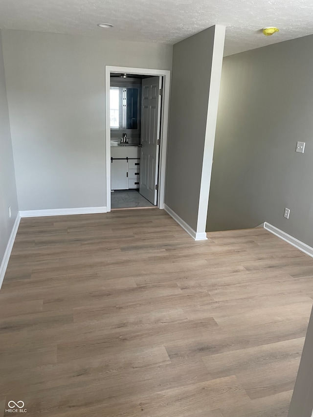 empty room with sink, a textured ceiling, and light wood-type flooring