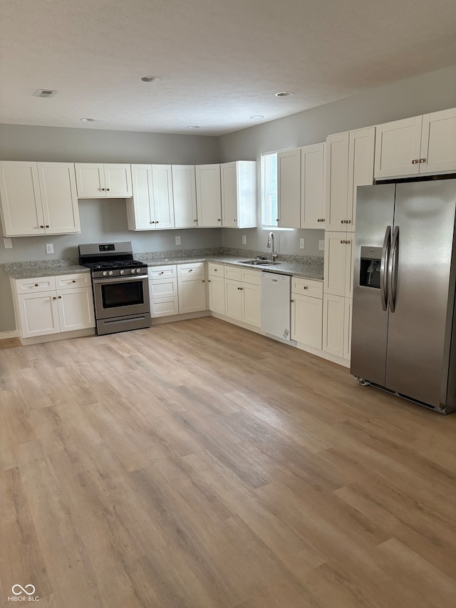 kitchen with appliances with stainless steel finishes, white cabinets, sink, and light hardwood / wood-style floors