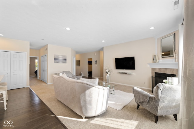 living room featuring a tiled fireplace, wood-type flooring, and a healthy amount of sunlight