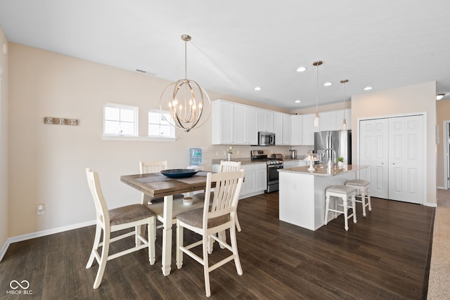 kitchen with white cabinets, a center island with sink, appliances with stainless steel finishes, dark wood-type flooring, and pendant lighting