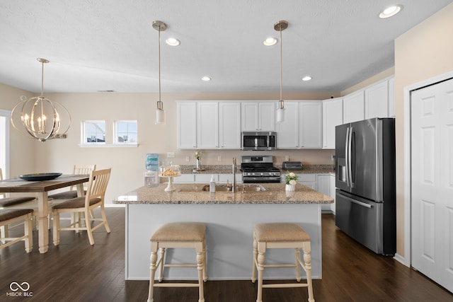 kitchen featuring appliances with stainless steel finishes, decorative light fixtures, white cabinets, light stone counters, and dark hardwood / wood-style floors