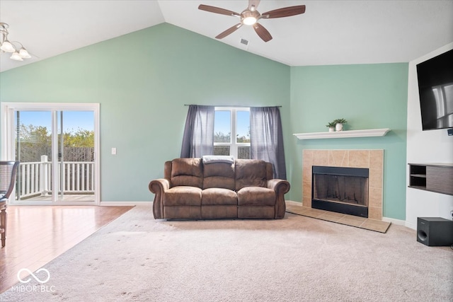 living room featuring a tiled fireplace, a healthy amount of sunlight, wood-type flooring, and vaulted ceiling