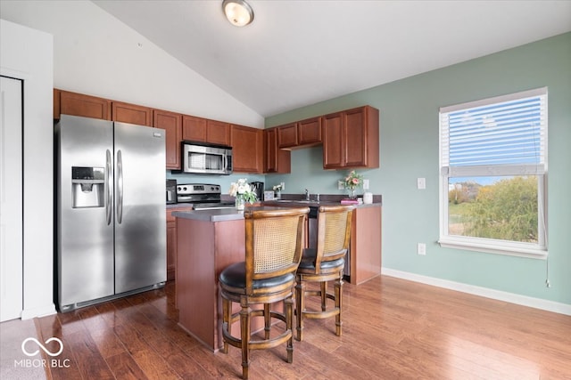 kitchen with dark hardwood / wood-style floors, stainless steel appliances, vaulted ceiling, a center island, and a kitchen bar