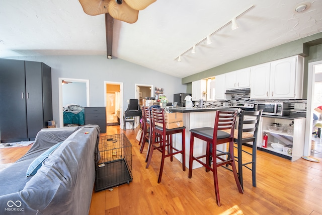 kitchen featuring light wood-type flooring, stainless steel appliances, white cabinets, and a breakfast bar area