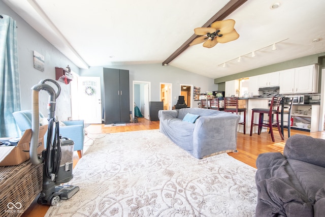 living room featuring light hardwood / wood-style floors, vaulted ceiling with beams, and ceiling fan