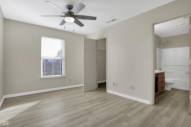 unfurnished bedroom with a closet, a walk in closet, ensuite bath, light wood-type flooring, and ceiling fan