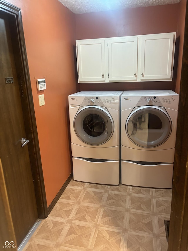 laundry room featuring cabinets, a textured ceiling, light parquet floors, and separate washer and dryer