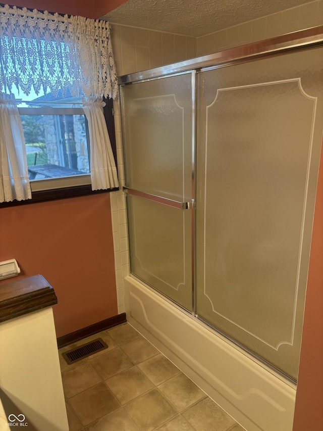 bathroom featuring a textured ceiling, tile patterned flooring, and bath / shower combo with glass door