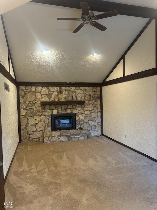 unfurnished living room featuring lofted ceiling, a textured ceiling, a stone fireplace, and carpet floors