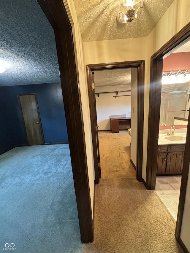 hallway featuring sink, a textured ceiling, and light colored carpet