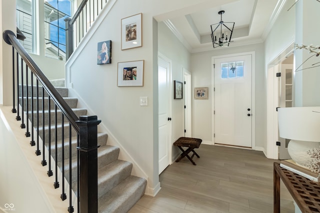 foyer entrance featuring an inviting chandelier, wood-type flooring, a tray ceiling, and crown molding