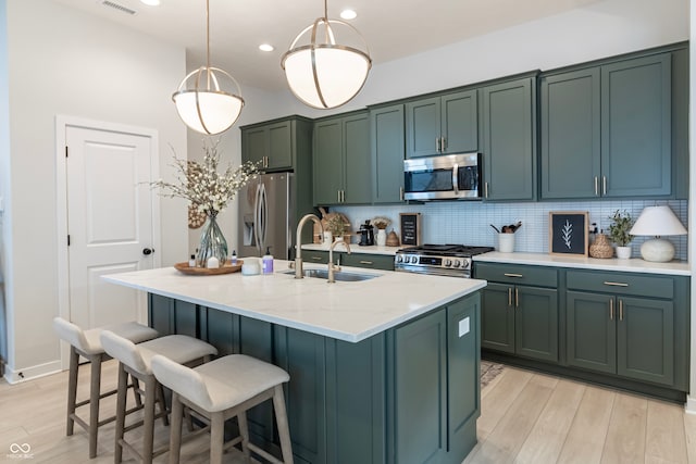 kitchen with light stone countertops, appliances with stainless steel finishes, light wood-type flooring, hanging light fixtures, and a center island with sink