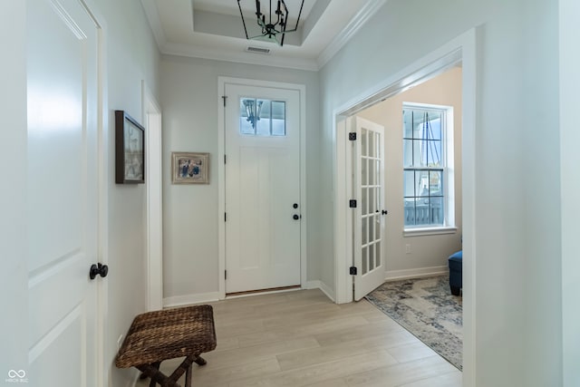 doorway to outside featuring light hardwood / wood-style flooring, a notable chandelier, crown molding, and a raised ceiling