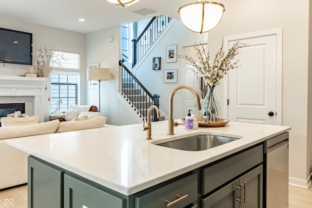 kitchen with sink, dishwasher, pendant lighting, light hardwood / wood-style flooring, and a center island with sink