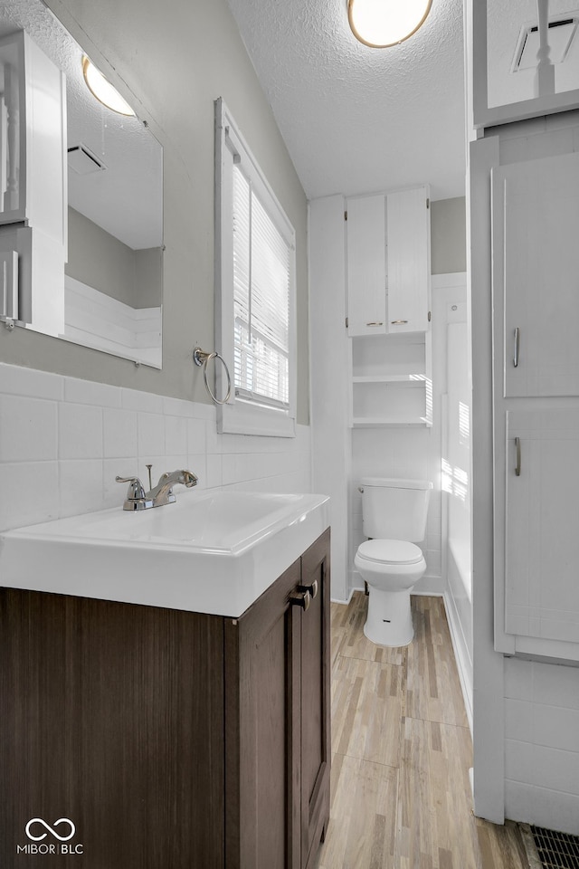 bathroom with wood-type flooring, backsplash, a textured ceiling, toilet, and vanity