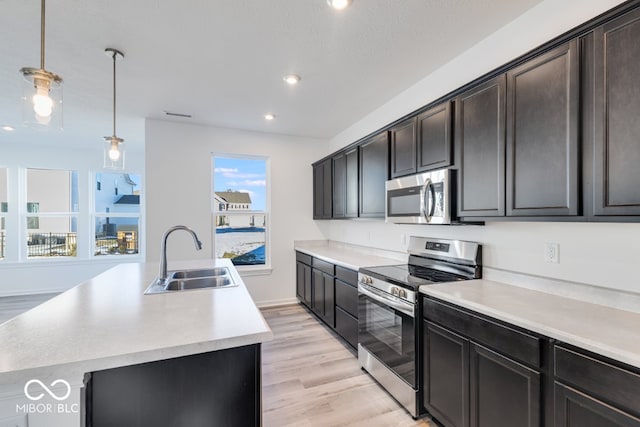 kitchen with stainless steel appliances, sink, decorative light fixtures, and an island with sink