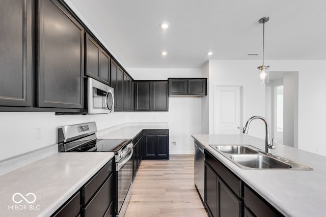 kitchen featuring appliances with stainless steel finishes, decorative light fixtures, sink, light hardwood / wood-style floors, and dark brown cabinets