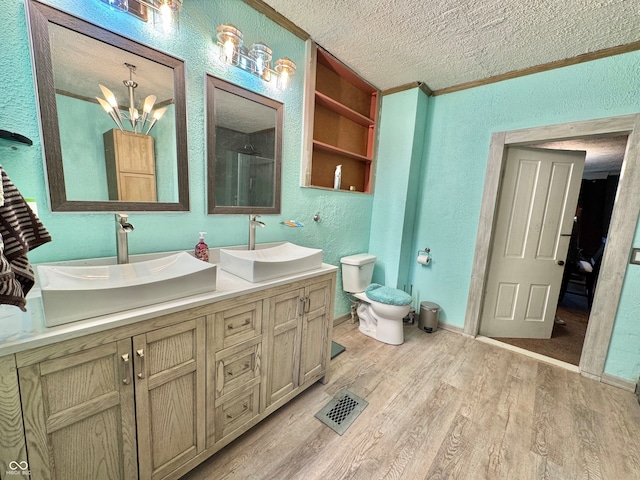 bathroom with wood-type flooring, a textured ceiling, toilet, vanity, and crown molding