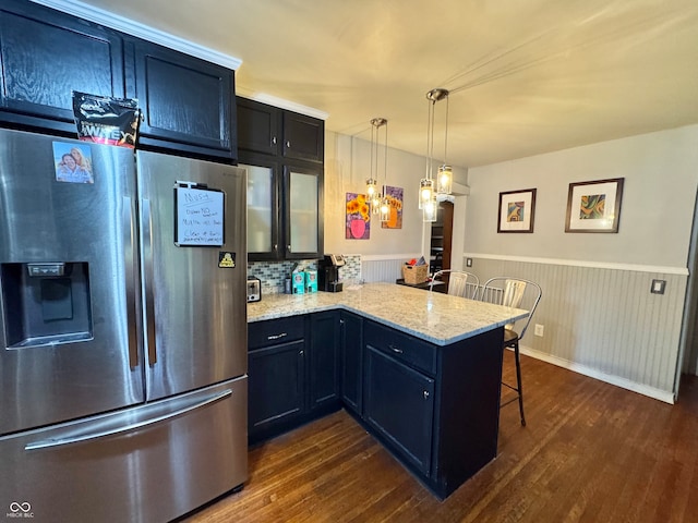 kitchen with a kitchen breakfast bar, dark wood-type flooring, stainless steel refrigerator with ice dispenser, kitchen peninsula, and light stone counters