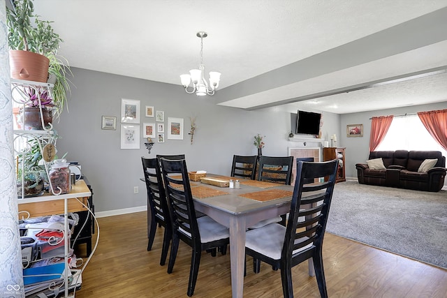 dining space featuring an inviting chandelier, wood-type flooring, a tiled fireplace, and a textured ceiling