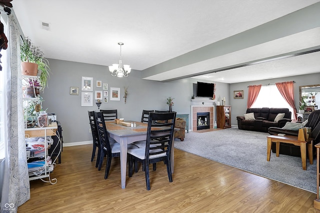 dining space featuring a tile fireplace, a chandelier, and light hardwood / wood-style floors