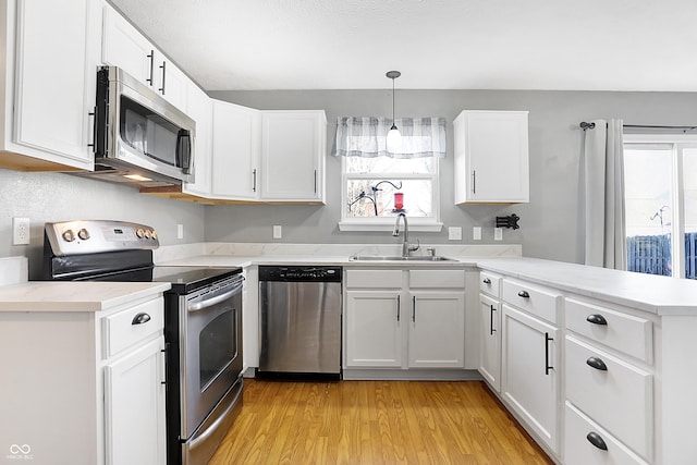 kitchen with white cabinetry, stainless steel appliances, sink, and hanging light fixtures