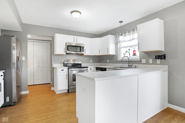 kitchen featuring sink, white cabinetry, hanging light fixtures, stainless steel appliances, and kitchen peninsula