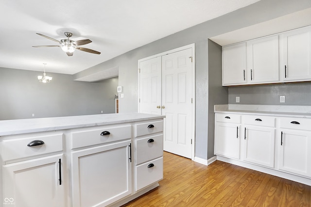 kitchen featuring white cabinetry, light stone countertops, ceiling fan with notable chandelier, and light wood-type flooring