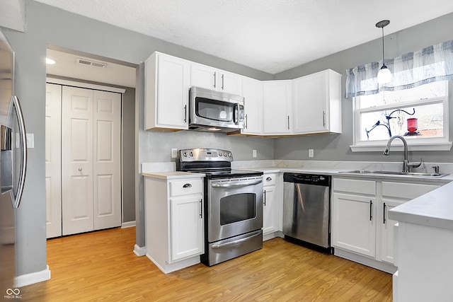 kitchen featuring sink, appliances with stainless steel finishes, white cabinetry, hanging light fixtures, and light hardwood / wood-style floors