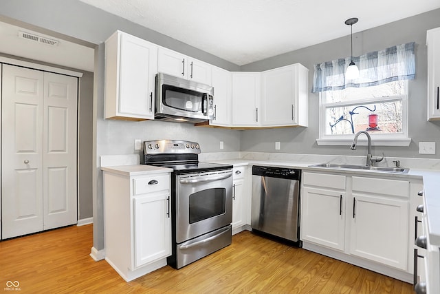 kitchen featuring pendant lighting, sink, stainless steel appliances, white cabinets, and light wood-type flooring