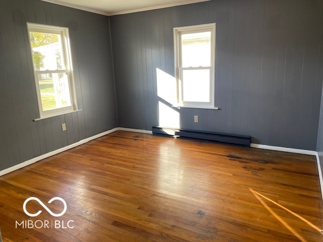 empty room featuring wood walls, hardwood / wood-style flooring, ornamental molding, and a baseboard radiator