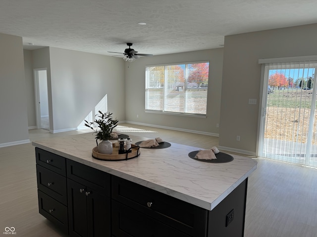 kitchen with ceiling fan, light hardwood / wood-style flooring, a center island, and a textured ceiling