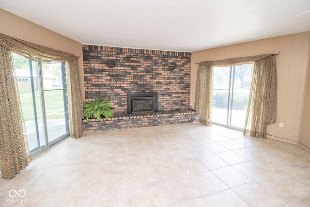 unfurnished living room with light tile patterned floors, brick wall, a healthy amount of sunlight, and a wood stove