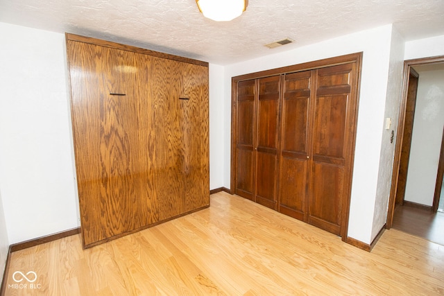 corridor with a textured ceiling and light hardwood / wood-style floors