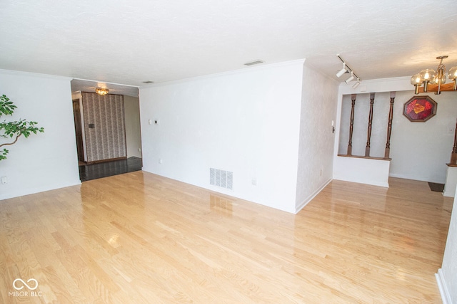 spare room with light wood-type flooring, a textured ceiling, rail lighting, crown molding, and an inviting chandelier