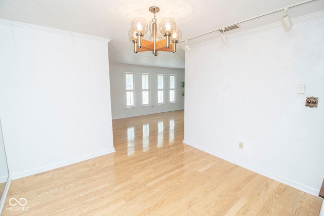 unfurnished room featuring crown molding, track lighting, a notable chandelier, and wood-type flooring