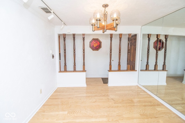 interior space with an inviting chandelier, crown molding, hardwood / wood-style floors, and rail lighting