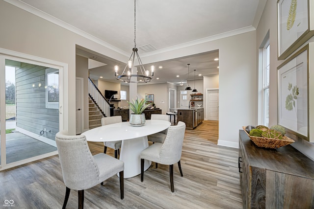 dining area with light hardwood / wood-style floors, ornamental molding, and a notable chandelier