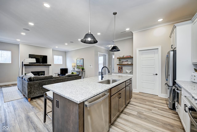 kitchen featuring sink, stainless steel appliances, a fireplace, white cabinets, and a center island with sink