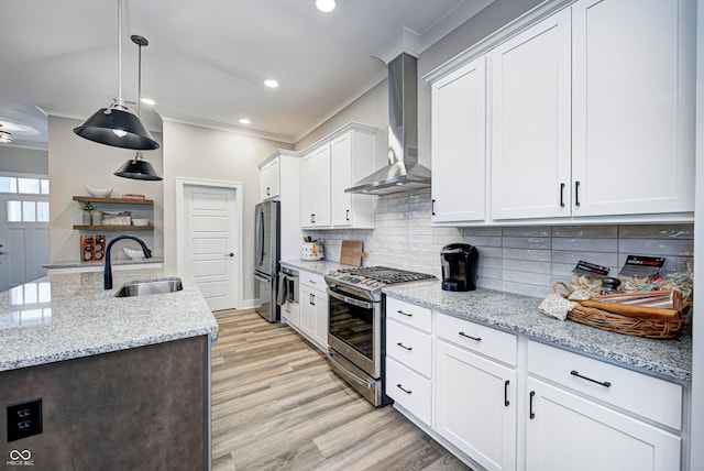 kitchen with pendant lighting, white cabinets, sink, wall chimney exhaust hood, and appliances with stainless steel finishes