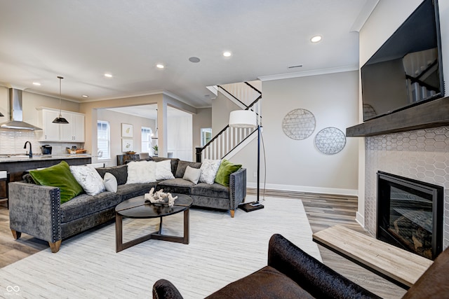 living room featuring light wood-type flooring, ornamental molding, and a tiled fireplace