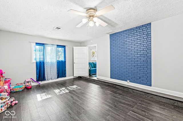 empty room featuring brick wall, hardwood / wood-style floors, a textured ceiling, and ceiling fan