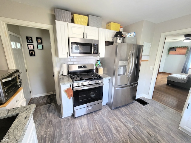 kitchen featuring appliances with stainless steel finishes, white cabinets, light stone countertops, and wood-type flooring