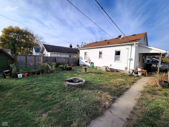 rear view of house with central air condition unit, a lawn, and a fire pit